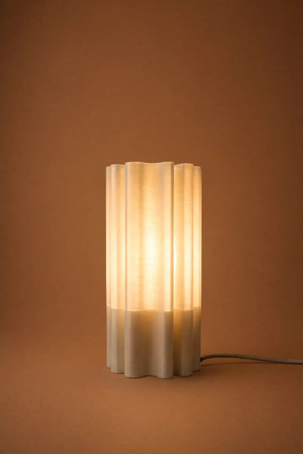 Lampe à poser Diplo allumée diffusant une lumière douce et chaleureuse à travers sa structure ondulée imprimée en 3D.