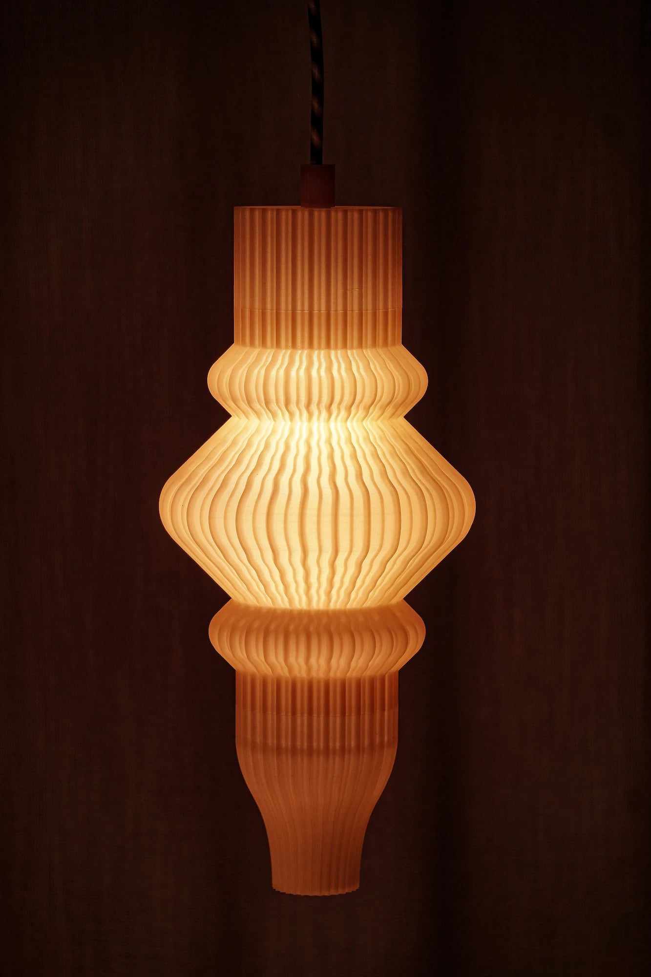 Suspension Vira diffusant une lumière douce à travers une matière biosourcée imprimée en 3D.